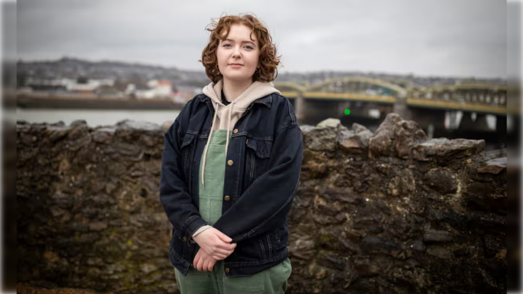 Alice Oseman a caucasian redhaired young woman photographed against a background of a bridge.