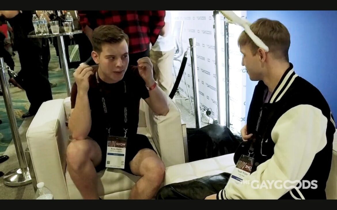 Screen Shot 2024 04 16 At 8.17.55 Pm Ryan Russo, a young male with dark short hair, has his hands right next to his phase as if saying his mind is blown. He is speaking to Noah White, a young blonde male with bunny rabbit ears. They are sitting on white leather coaches with a blue background.