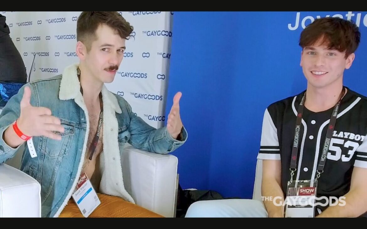 Jonah Wheeler, a brunette bearded man is facing the camera. He is wearing a denim jacket with sheep skin lining. He has no shirt underneath and a hairy chest. He is sitting next to Tyler Tanner, a smiling young man with a black and white shirt saying "Playboy 53".