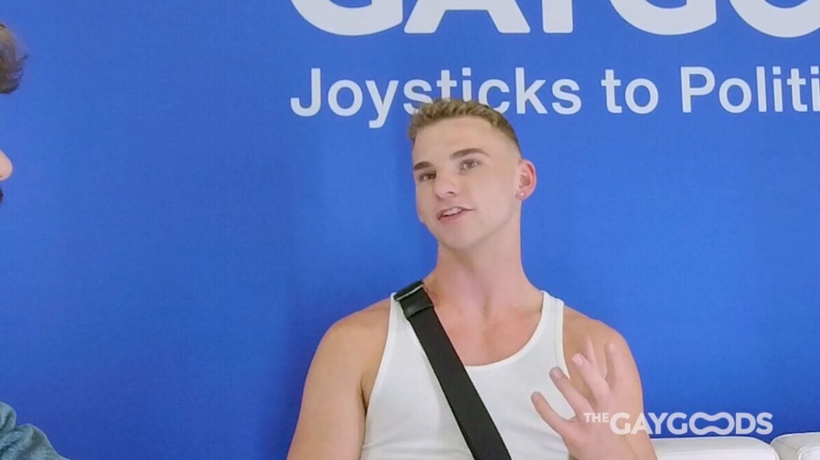 Screenshot 2024 05 15 221044 Blonde haired Jack Waters is speaking to Jonah Wheeler off-screen. He is sitting in from of a blue backdrop with the words "Joysticks to Politi-" written in white writing. He's wearing a white tank top and has a black bag strap over his right shoulder.
