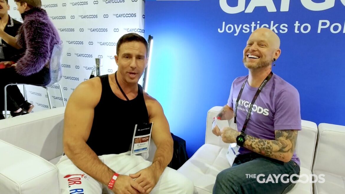 Reese Rideout, a bronze skinned hunk wearing a black tank top and white pants is facing the camera. Justin Carnal, with a purple T-shirt and tattoos is laughing next to him. Reese looks like he's attempting "Blue Steel" from the movie Zoolander. His pants have the words "Dr Rideout" in red, with an exploding thermometer image on them. God knows why